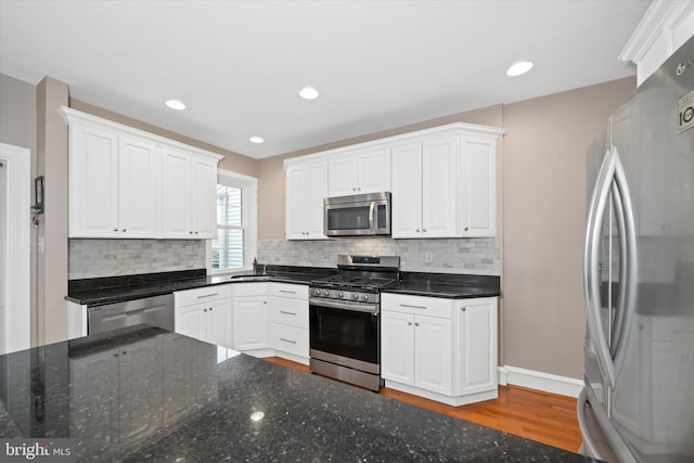 kitchen with white cabinetry, wood finished floors, backsplash, and stainless steel appliances