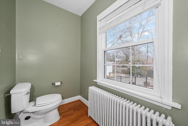 bathroom featuring baseboards, radiator, wood finished floors, and toilet