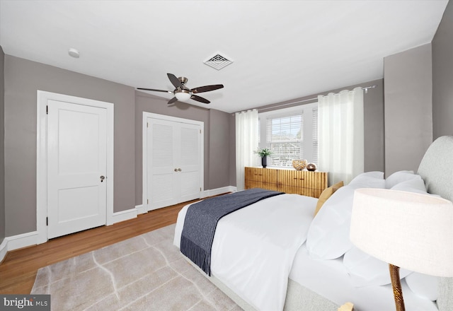 bedroom with ceiling fan, wood finished floors, visible vents, and baseboards