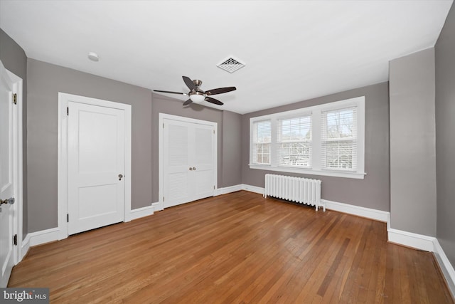 unfurnished bedroom featuring light wood-style floors, visible vents, radiator heating unit, and baseboards