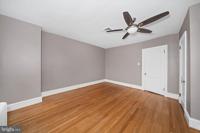 spare room featuring visible vents, baseboards, ceiling fan, radiator heating unit, and light wood-style flooring