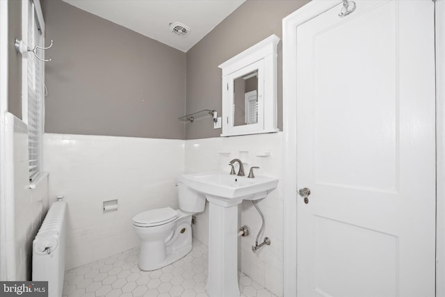 half bath featuring radiator, visible vents, tile walls, toilet, and tile patterned floors