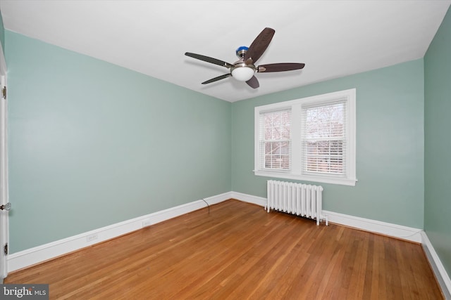 empty room featuring ceiling fan, baseboards, wood finished floors, and radiator heating unit