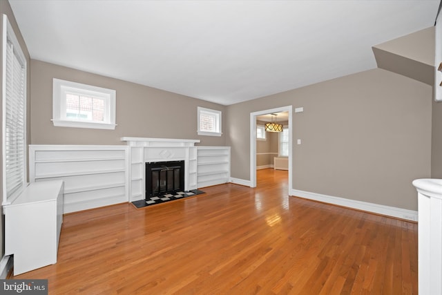 unfurnished living room featuring a fireplace with flush hearth, wood finished floors, and baseboards