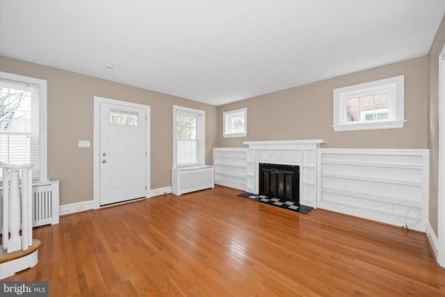 unfurnished living room with a fireplace, radiator heating unit, wood finished floors, and baseboards