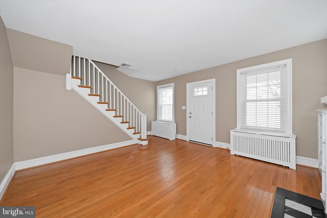 entryway featuring baseboards, visible vents, light wood finished floors, radiator heating unit, and stairs