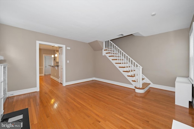 unfurnished living room featuring stairway, wood finished floors, visible vents, and baseboards