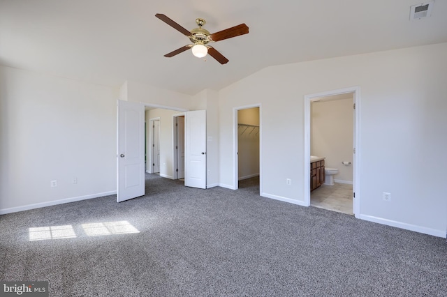 unfurnished bedroom featuring visible vents, a walk in closet, lofted ceiling, carpet flooring, and ensuite bath