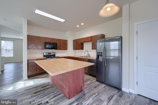 kitchen featuring wood finished floors, a sink, black appliances, wood counters, and a center island