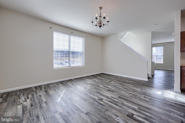 unfurnished living room with a wealth of natural light, dark wood-style floors, baseboards, and a notable chandelier