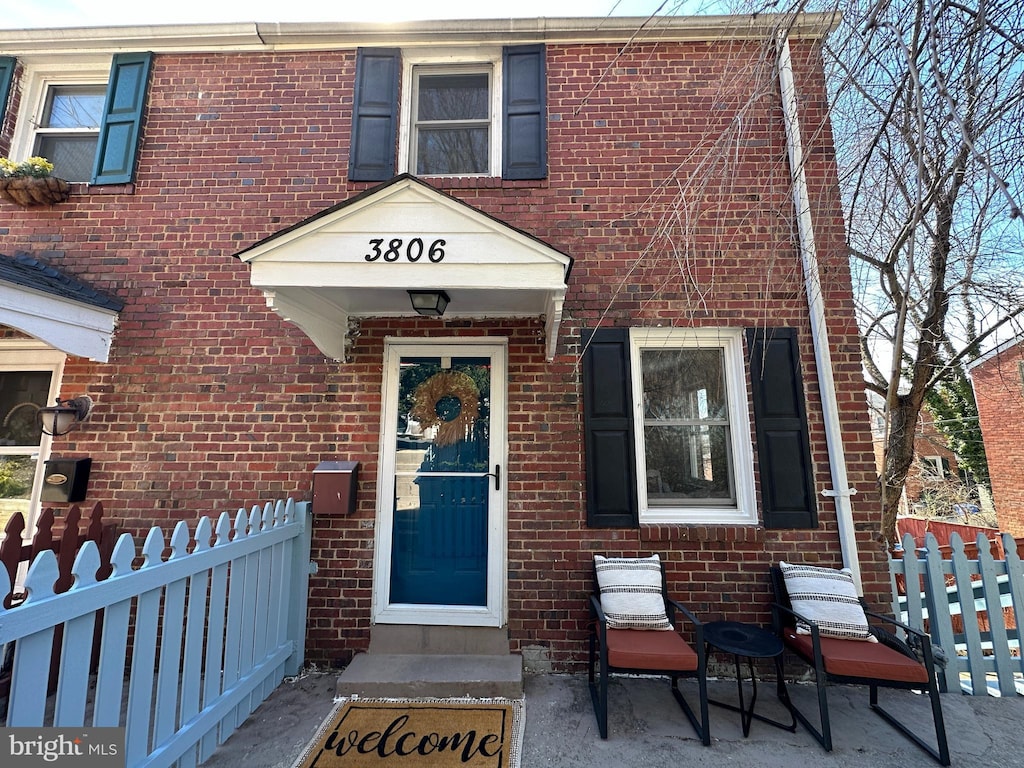 view of exterior entry featuring fence and brick siding