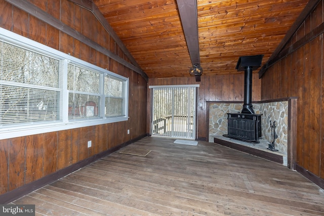 unfurnished living room with hardwood / wood-style floors, wood walls, wooden ceiling, a wood stove, and vaulted ceiling