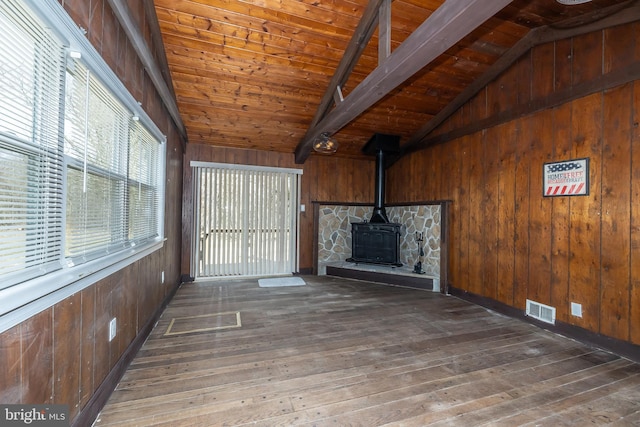 unfurnished living room with visible vents, wood walls, lofted ceiling with beams, and hardwood / wood-style flooring