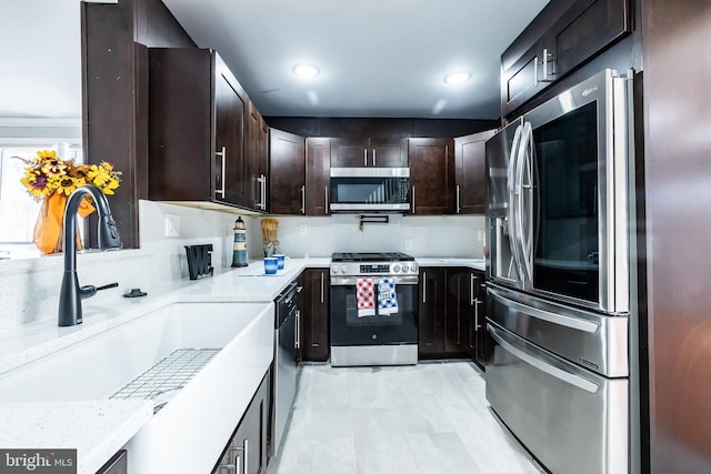 kitchen featuring light stone counters, recessed lighting, a sink, dark brown cabinetry, and appliances with stainless steel finishes