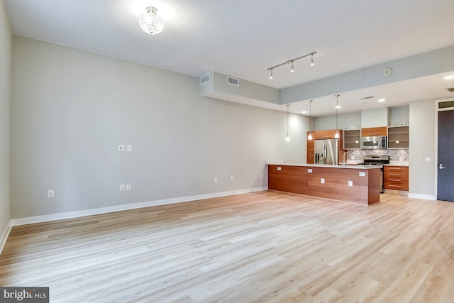 kitchen with brown cabinetry, baseboards, light wood finished floors, appliances with stainless steel finishes, and backsplash