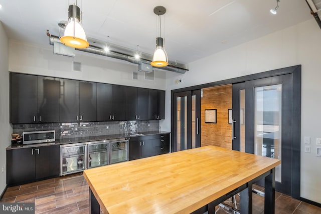 kitchen with stainless steel microwave, dark cabinetry, decorative backsplash, and hanging light fixtures