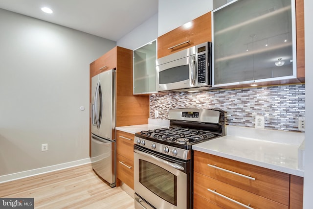 kitchen featuring light wood-type flooring, glass insert cabinets, appliances with stainless steel finishes, brown cabinetry, and decorative backsplash