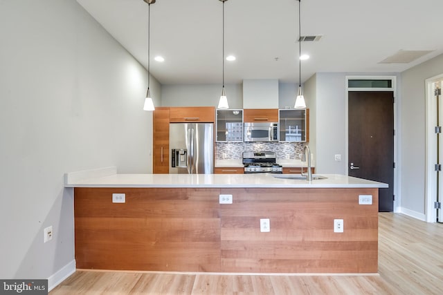 kitchen with tasteful backsplash, glass insert cabinets, light countertops, stainless steel appliances, and a sink