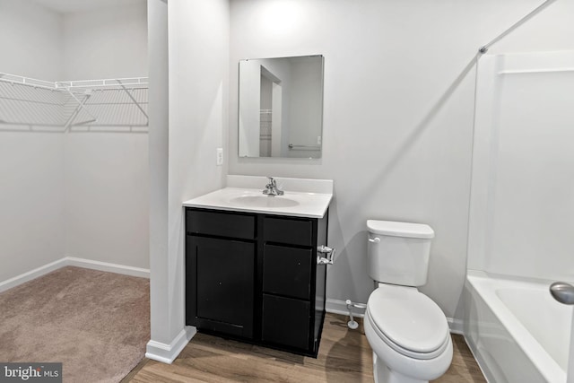 full bathroom featuring a walk in closet, toilet, vanity, and baseboards