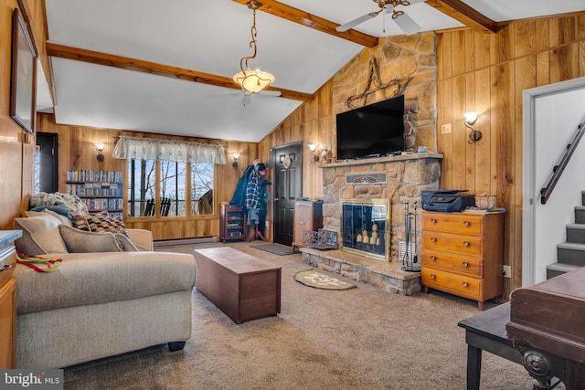 living room with wooden walls, ceiling fan, carpet, stairs, and a stone fireplace