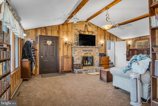 carpeted living area featuring stairway, wood walls, lofted ceiling with beams, a fireplace, and a ceiling fan