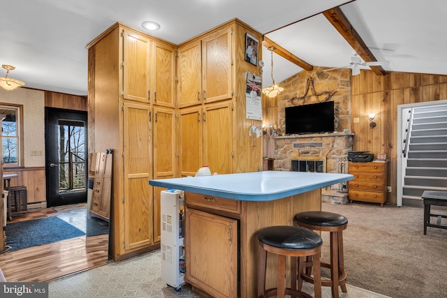 kitchen featuring open floor plan, a stone fireplace, wood walls, ceiling fan, and vaulted ceiling with beams