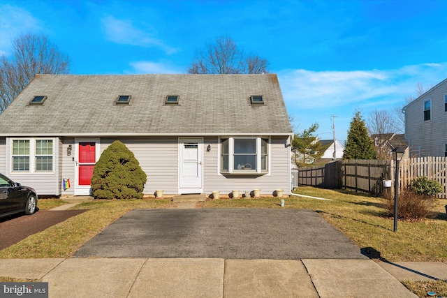 view of front facade with a front lawn, fence, and a shingled roof