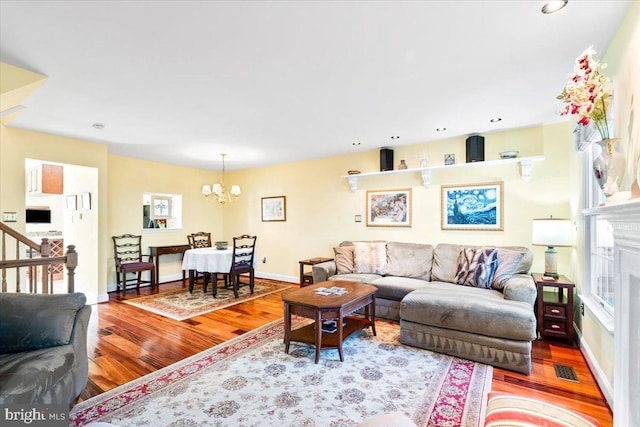 living room featuring wood finished floors, visible vents, baseboards, stairs, and a notable chandelier