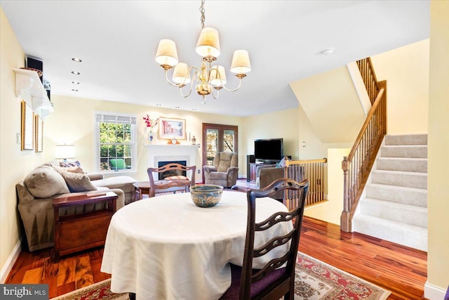 dining area featuring stairway, recessed lighting, a fireplace, wood finished floors, and a notable chandelier