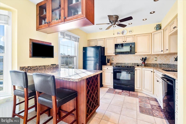 kitchen with tasteful backsplash, cream cabinets, black appliances, and a kitchen bar