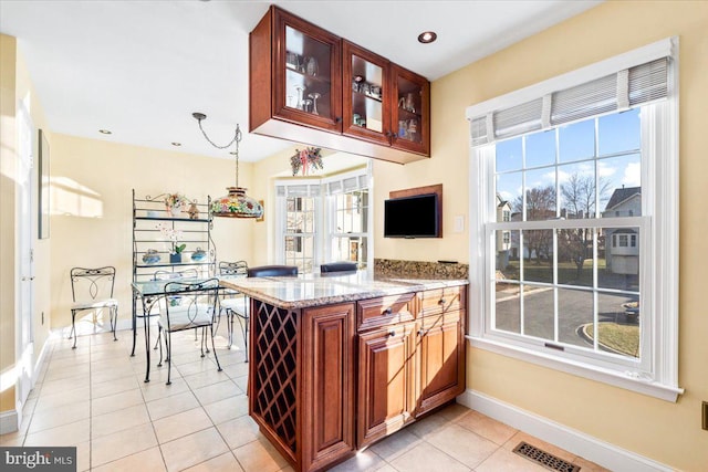 kitchen featuring light tile patterned floors, light stone countertops, visible vents, baseboards, and glass insert cabinets