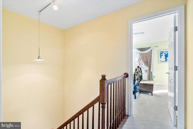 hall with track lighting, an upstairs landing, and carpet floors