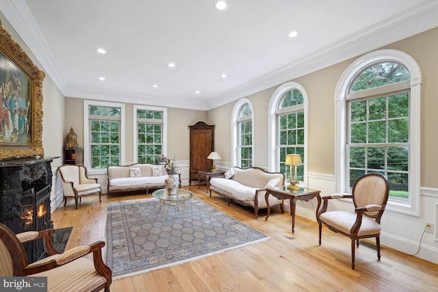 living area with wood finished floors, a healthy amount of sunlight, a wainscoted wall, and ornamental molding