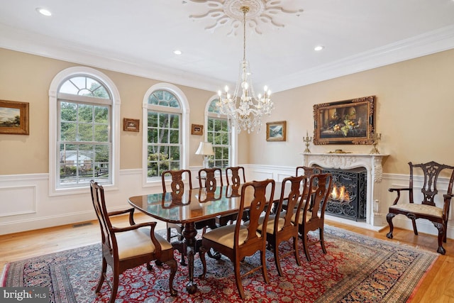 dining room with crown molding, light wood-type flooring, a wainscoted wall, and a premium fireplace