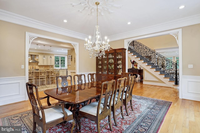 dining space featuring crown molding, stairway, light wood-style flooring, and a wainscoted wall