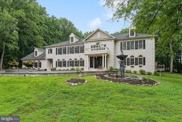 georgian-style home with brick siding, a balcony, and a front yard