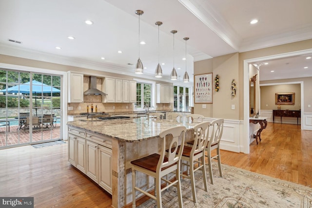 kitchen with light wood finished floors, visible vents, decorative backsplash, wainscoting, and wall chimney exhaust hood