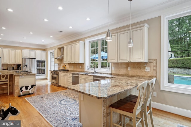 kitchen with a kitchen breakfast bar, wall chimney exhaust hood, light wood-style flooring, and stainless steel appliances