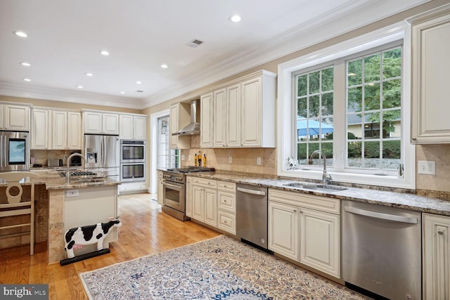 kitchen with wall chimney range hood, visible vents, appliances with stainless steel finishes, and a sink