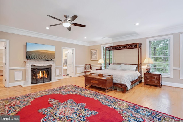 bedroom featuring wood finished floors, a fireplace with flush hearth, ornamental molding, and wainscoting