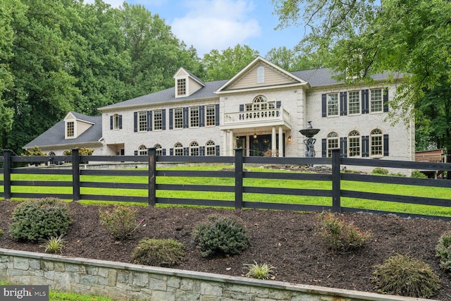 colonial house featuring a fenced front yard, a balcony, and brick siding