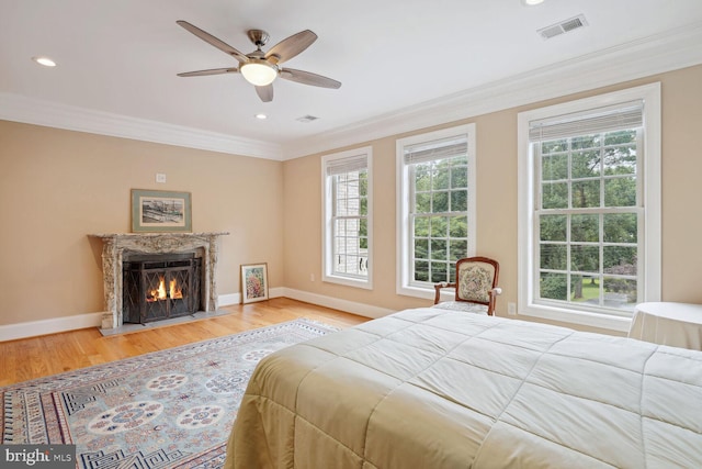 bedroom with a high end fireplace, visible vents, crown molding, baseboards, and wood finished floors