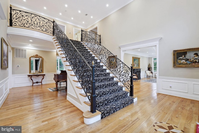 stairway featuring wood finished floors, visible vents, a fireplace, ornamental molding, and a decorative wall