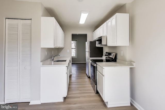 kitchen with light wood-type flooring, light countertops, white cabinets, stainless steel appliances, and a sink