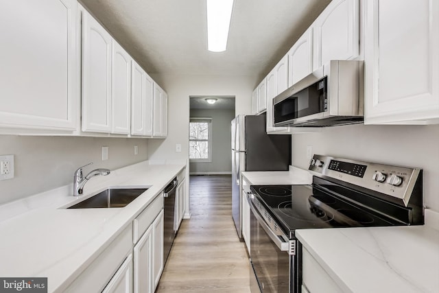 kitchen featuring a sink, stainless steel appliances, light stone counters, and white cabinetry