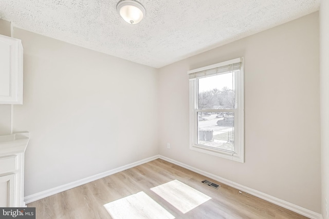 spare room featuring visible vents, baseboards, a textured ceiling, and light wood finished floors