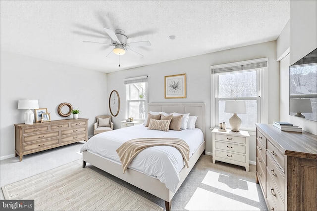 bedroom with ceiling fan, light colored carpet, baseboards, and a textured ceiling