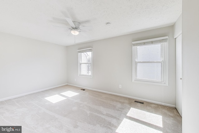 carpeted spare room with visible vents, baseboards, a textured ceiling, and a ceiling fan