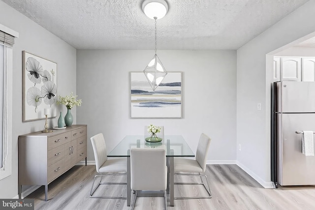 dining space featuring baseboards, a textured ceiling, and light wood finished floors