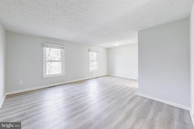 unfurnished room with visible vents, wood finished floors, baseboards, and a textured ceiling